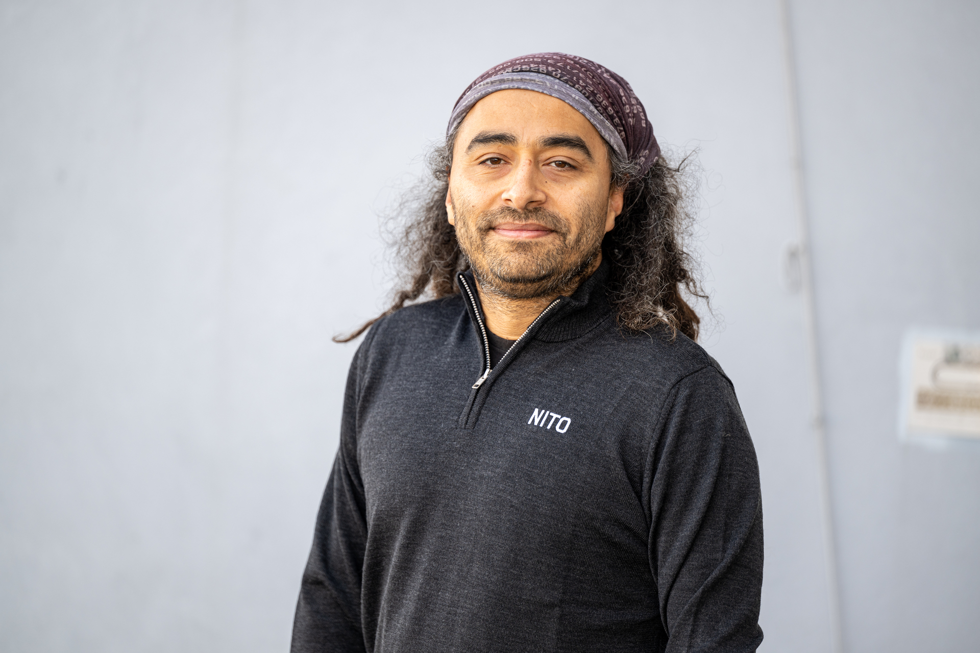 Mann med svart hår og skjegg har på seg NITO-genser. Står foran en hvit vegg