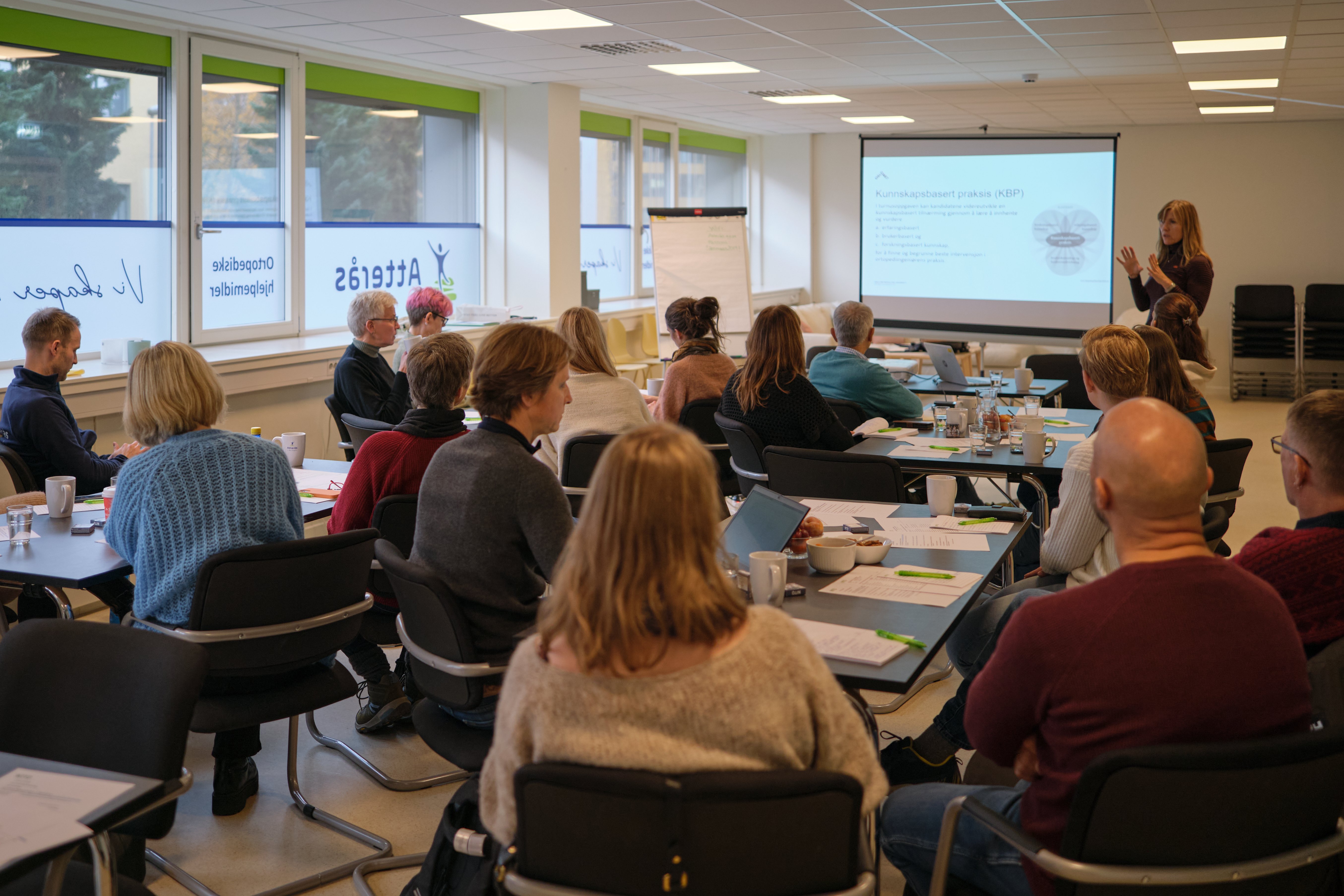Gruppe mennesker som sitter rundt små bord i ett klasserom