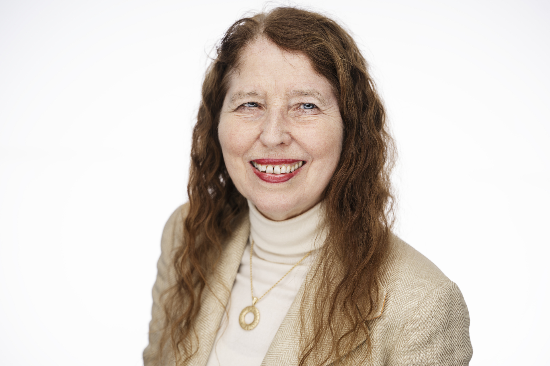 Dame med langt rødt hår, genser med høy hals og dressjakke. Ser rett i kamera. Bakgrunn hvit