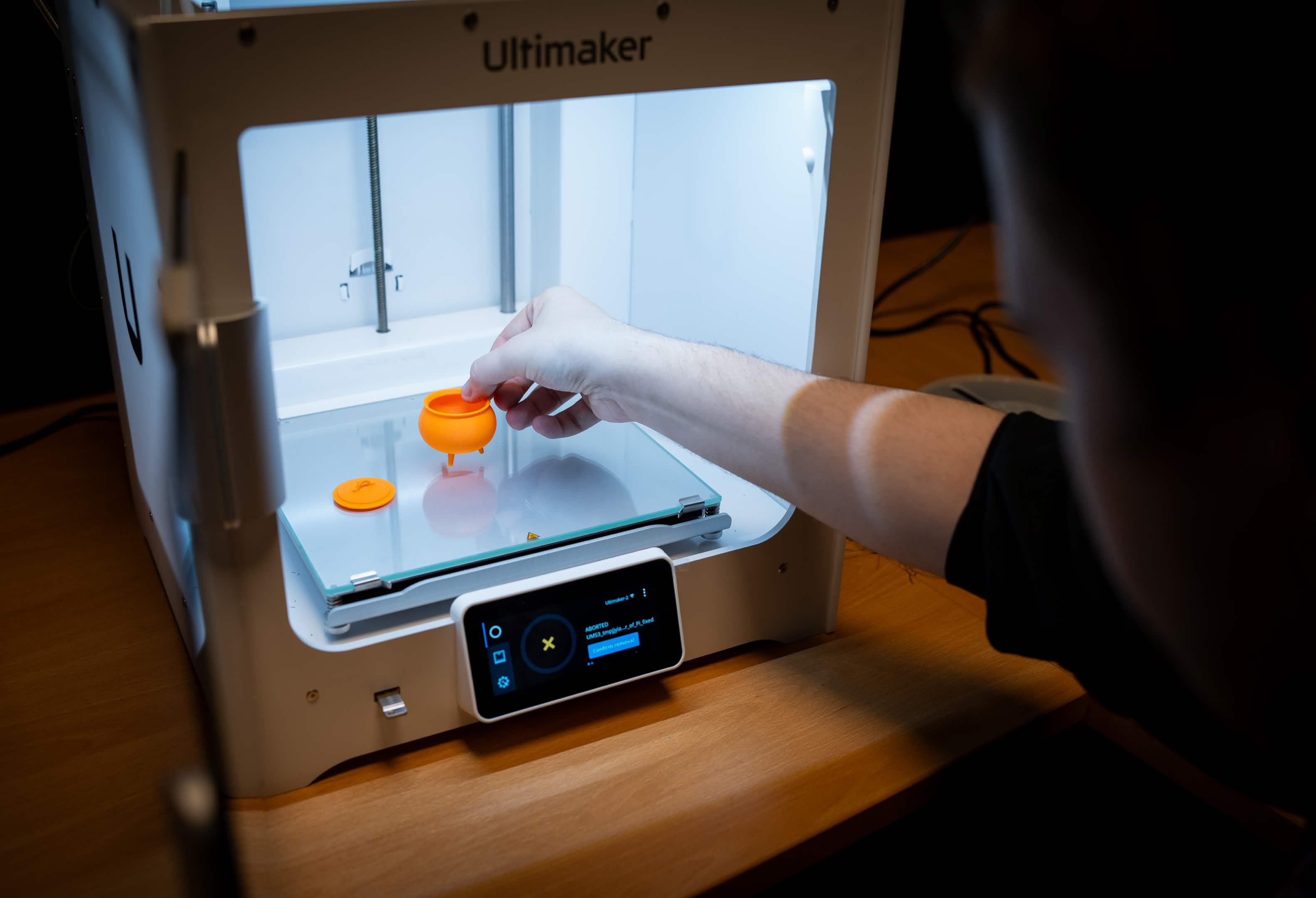 Image of a person taking an orange small 3D-printed model out of a 3D printer. Credit: Future Classroom