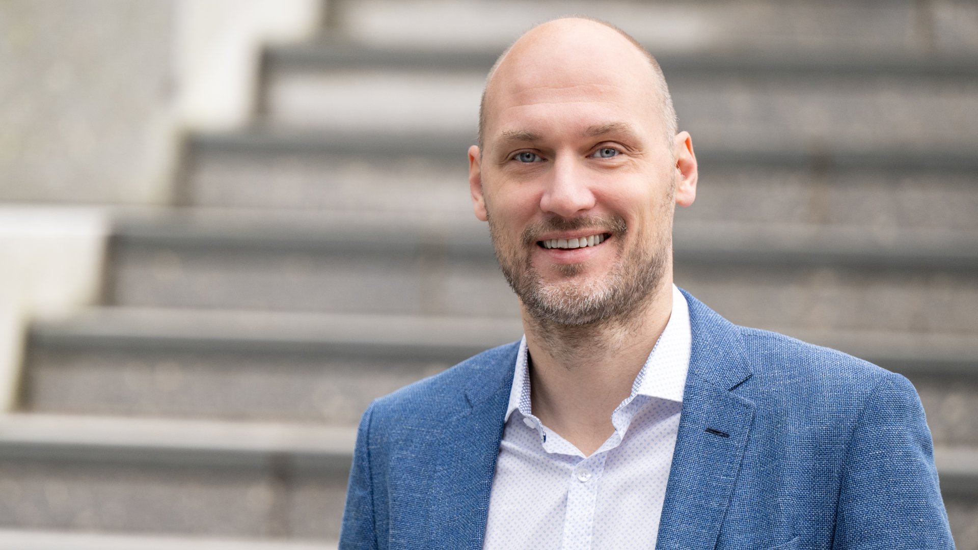 Mann med prikkete hvit skjorte og blå blazer som ser inn i kamera