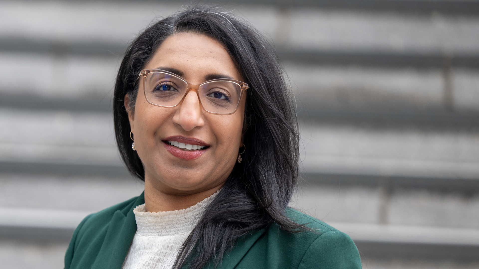 Kvinne med briller og mørkt hår, ikledd grønn jakke som ser inn i kamera