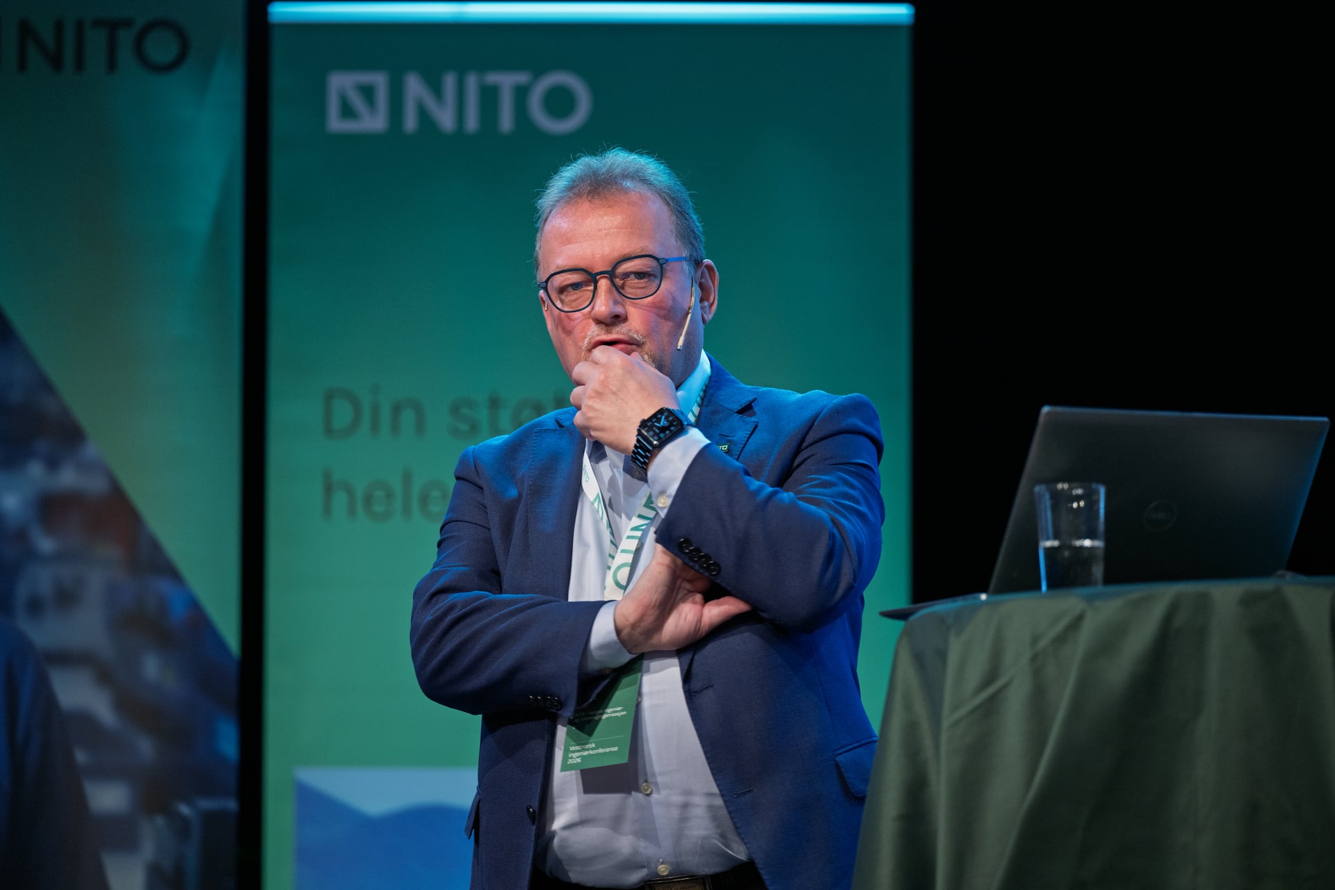 Mann med briller på scenen. Iført skjorte og jakke