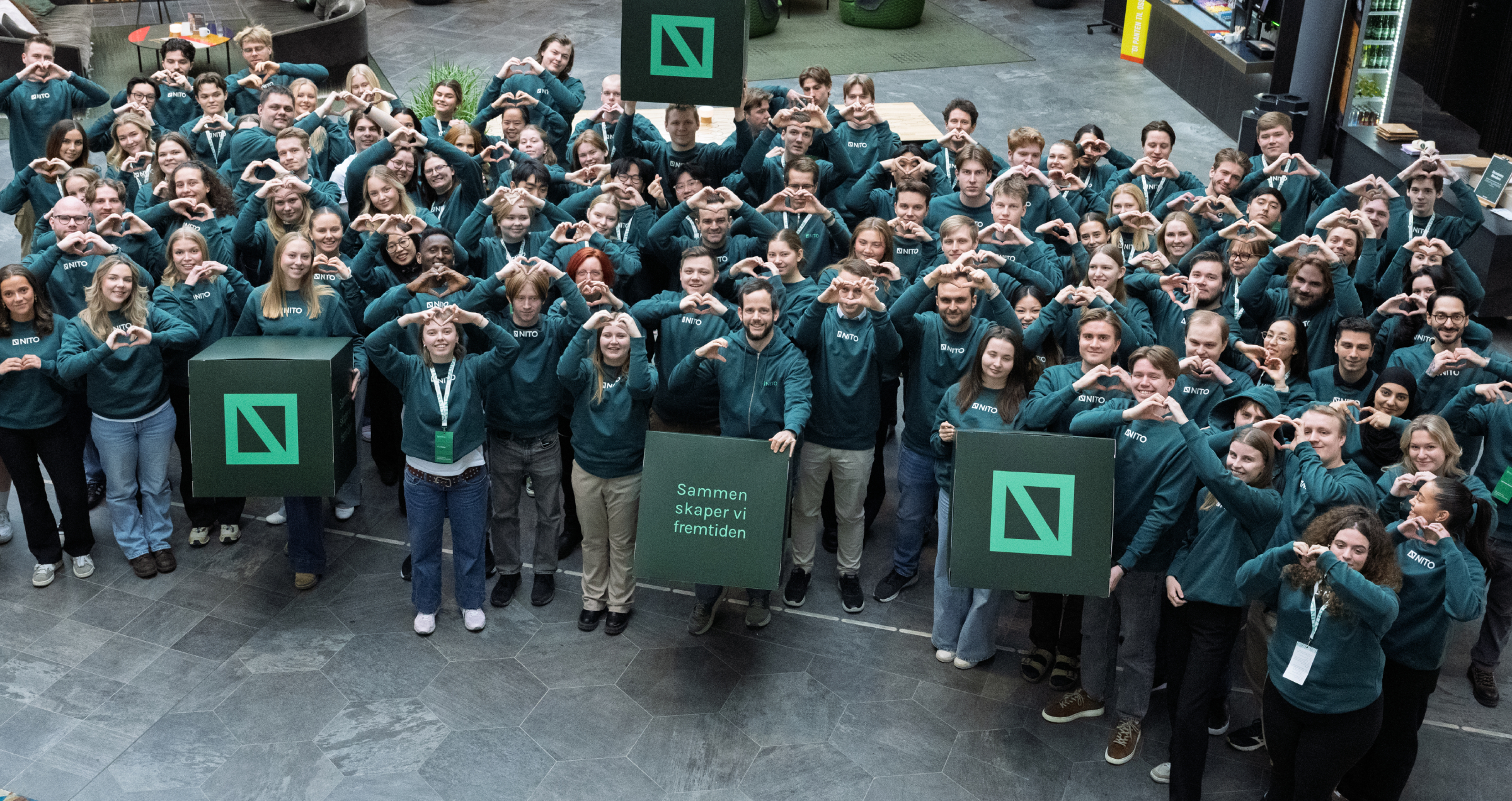 En stor gruppe unge i grønne NITO-gensere former hjerter med hendene.
