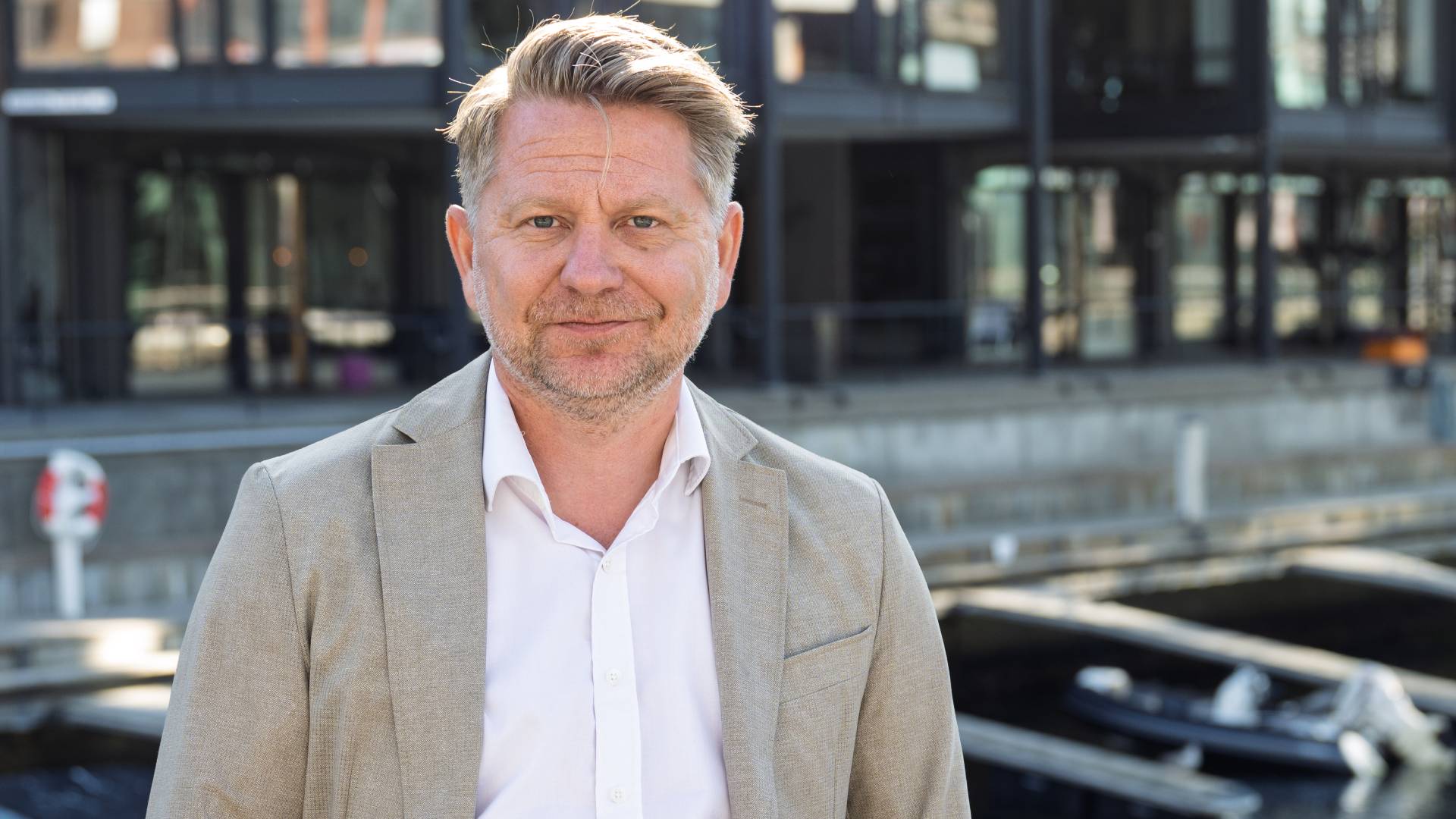 Mann i lys dressjakke foran moderne byarkitektur.
