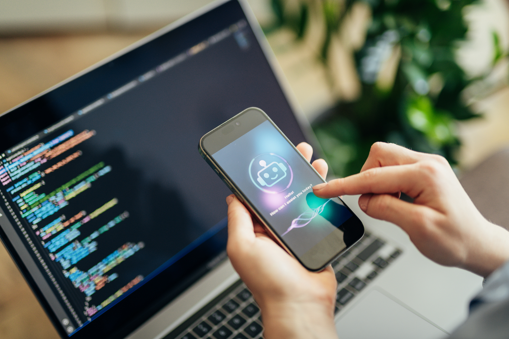 Forretningskvinne bruker AI-chatbot på telefonen mens hun jobber på laptop
