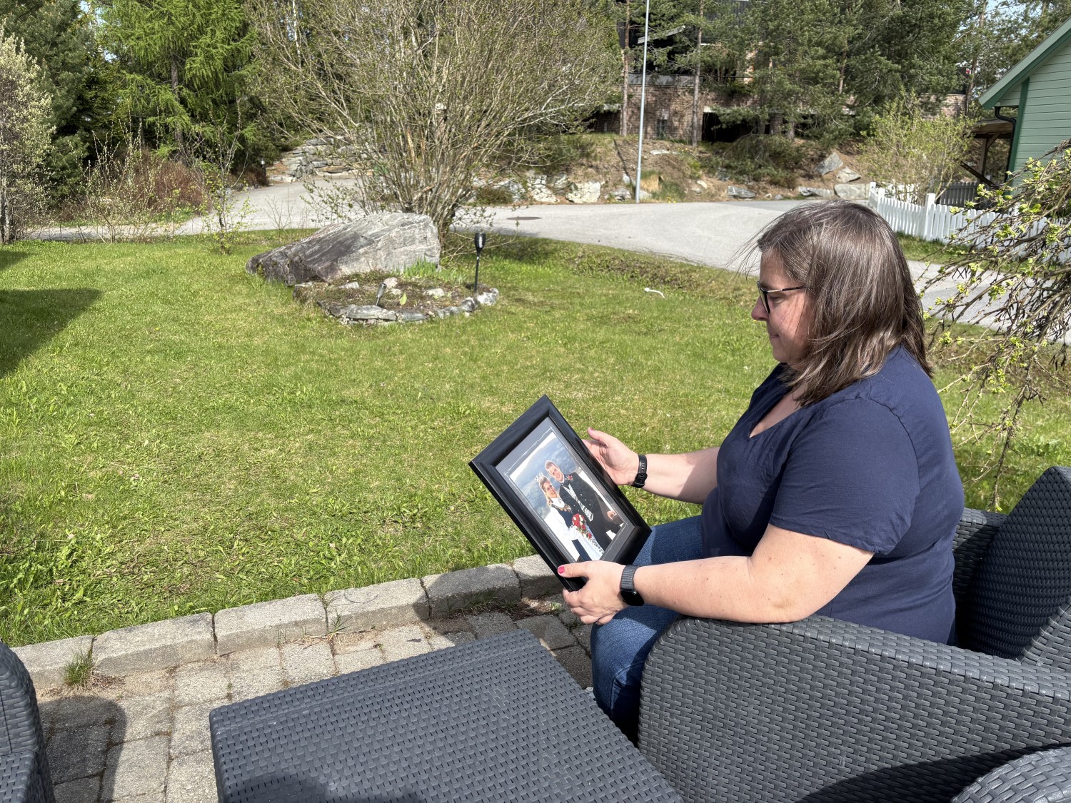 A woman with glasses sits outside on a terrace, using a tablet.