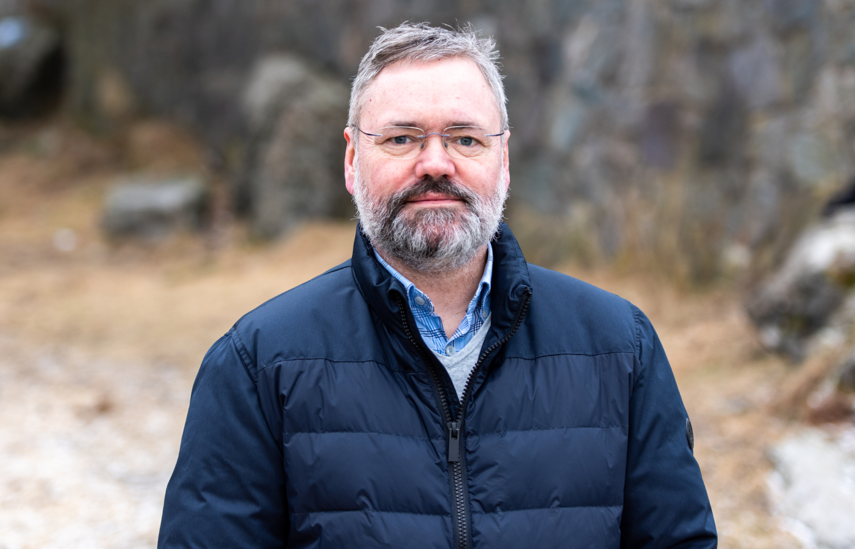 Bildet viser en voksen mann med briller og grått skjegg. Han har på seg mørk jakke og står utendørs foran en uklar bakgrunn.