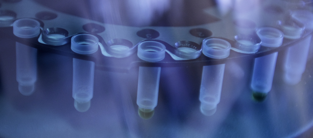 The image shows microcentrifuge tubes in a laboratory, used for storing biological samples such as DNA/RNA, under blue light.