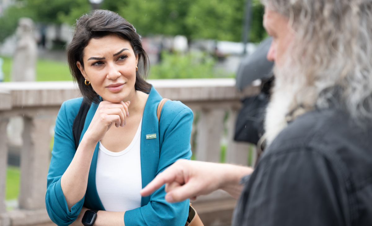 Kvinne i turkis blazer og mørkt hår, og en mann med langt grått hår