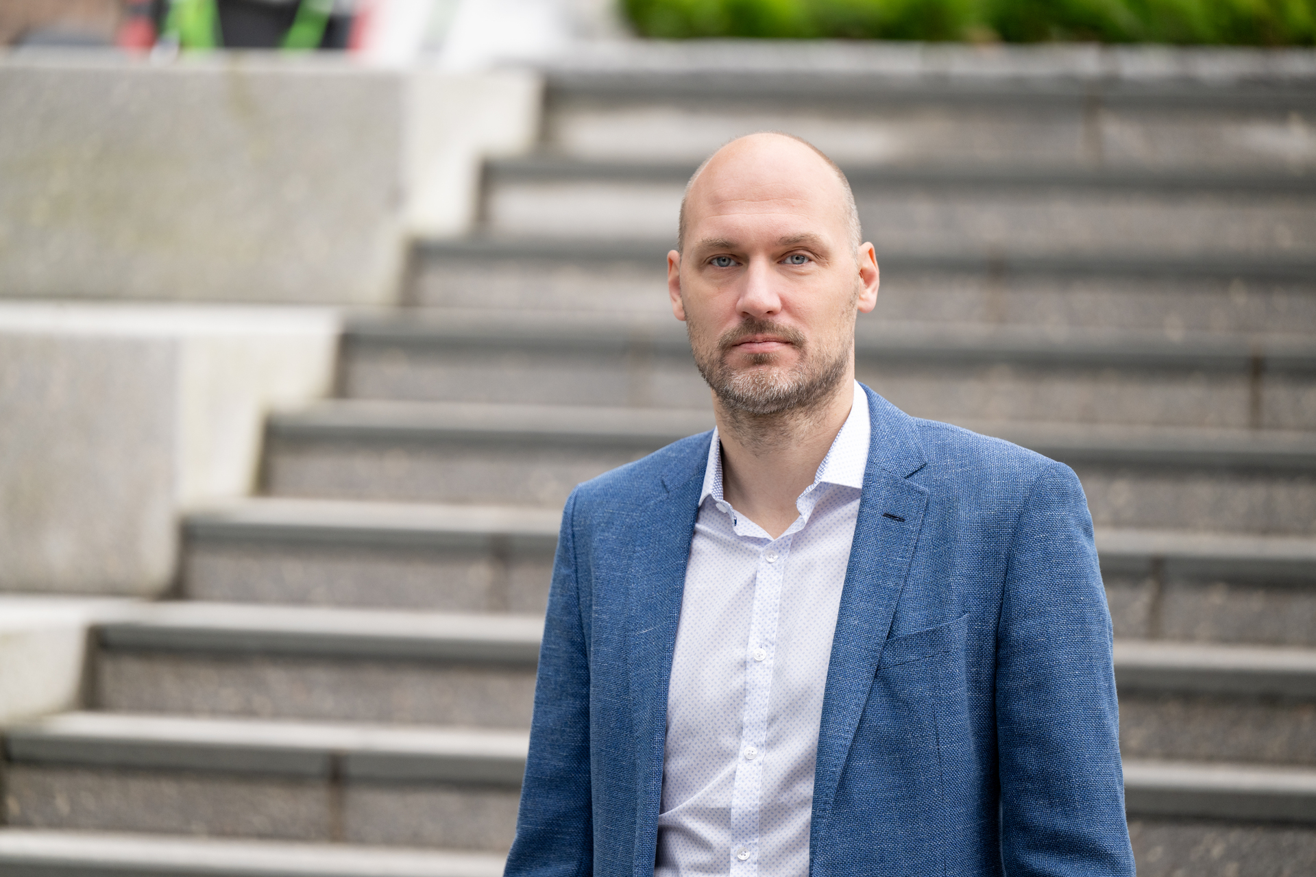 Mann står foran en trapp i hvit skjorte og blå blazer