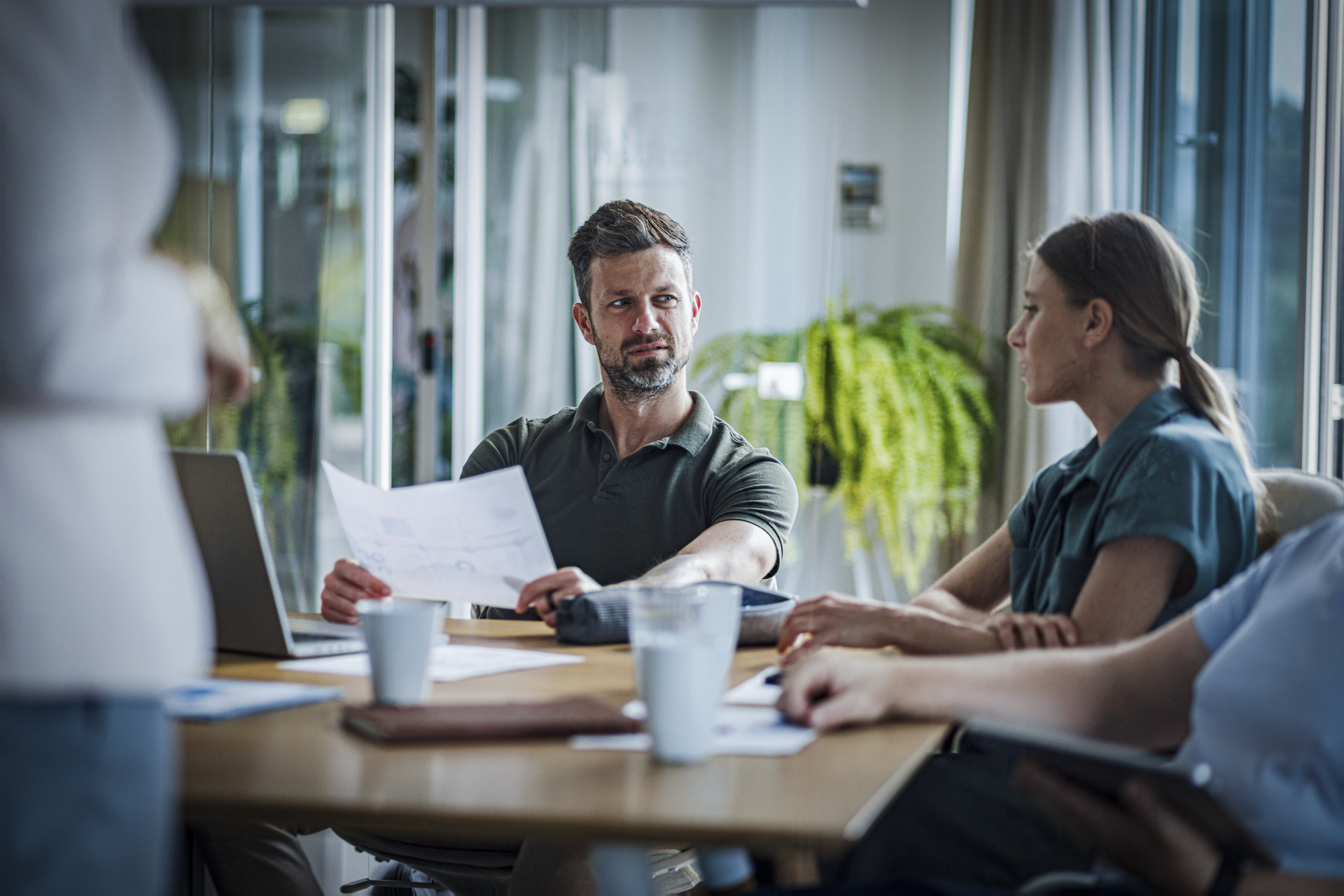 En voksen mann i kontorlandskap sitter ved et bord med dokumenter foran seg og ser ettertenksomt mot sin kvinnelige samtalepartner.