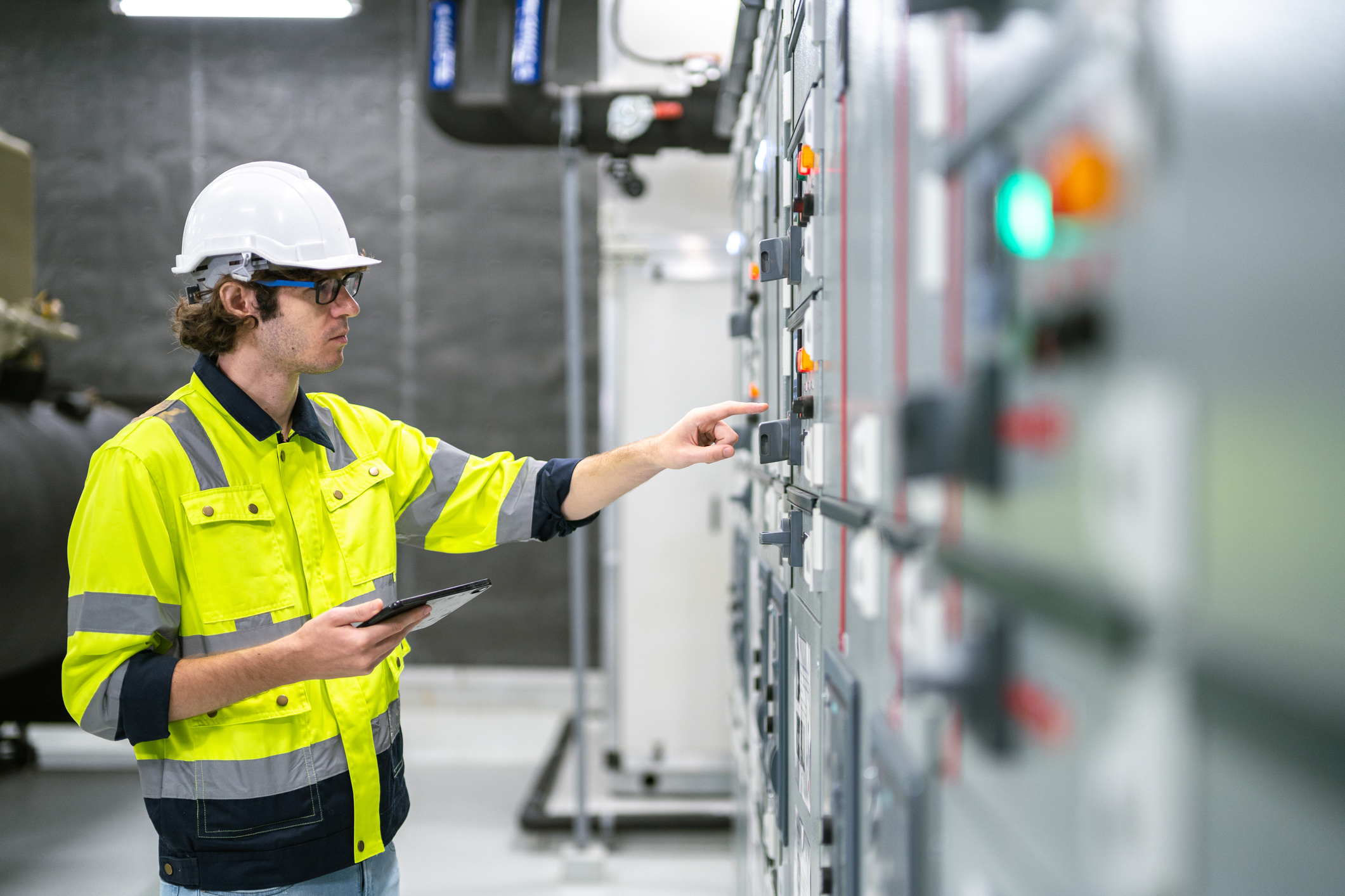 En person inspiserer og betjener et industrielt elektrisk kontrollpanel i et teknisk miljø