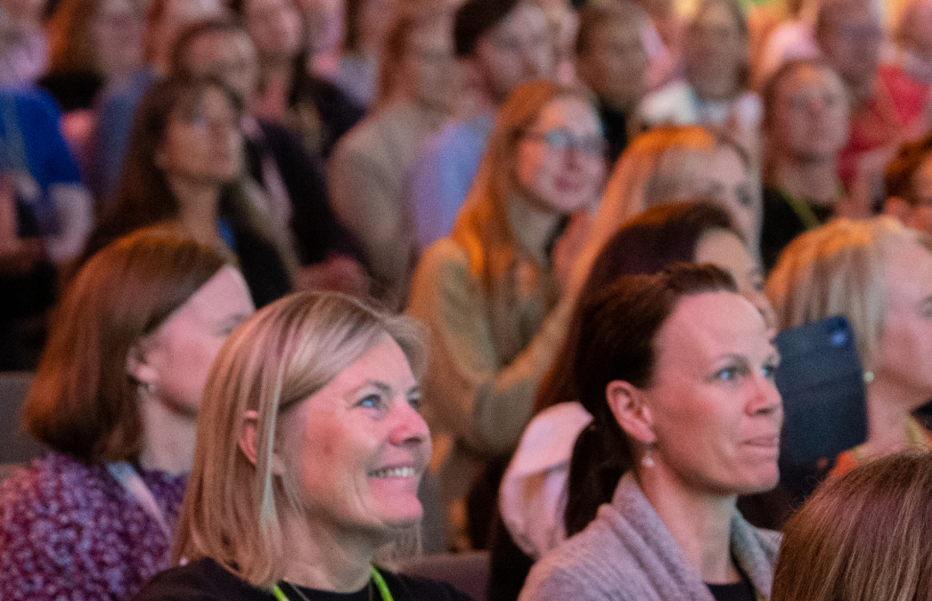 En gruppe blide mennesker som sitter i en kongressal. 