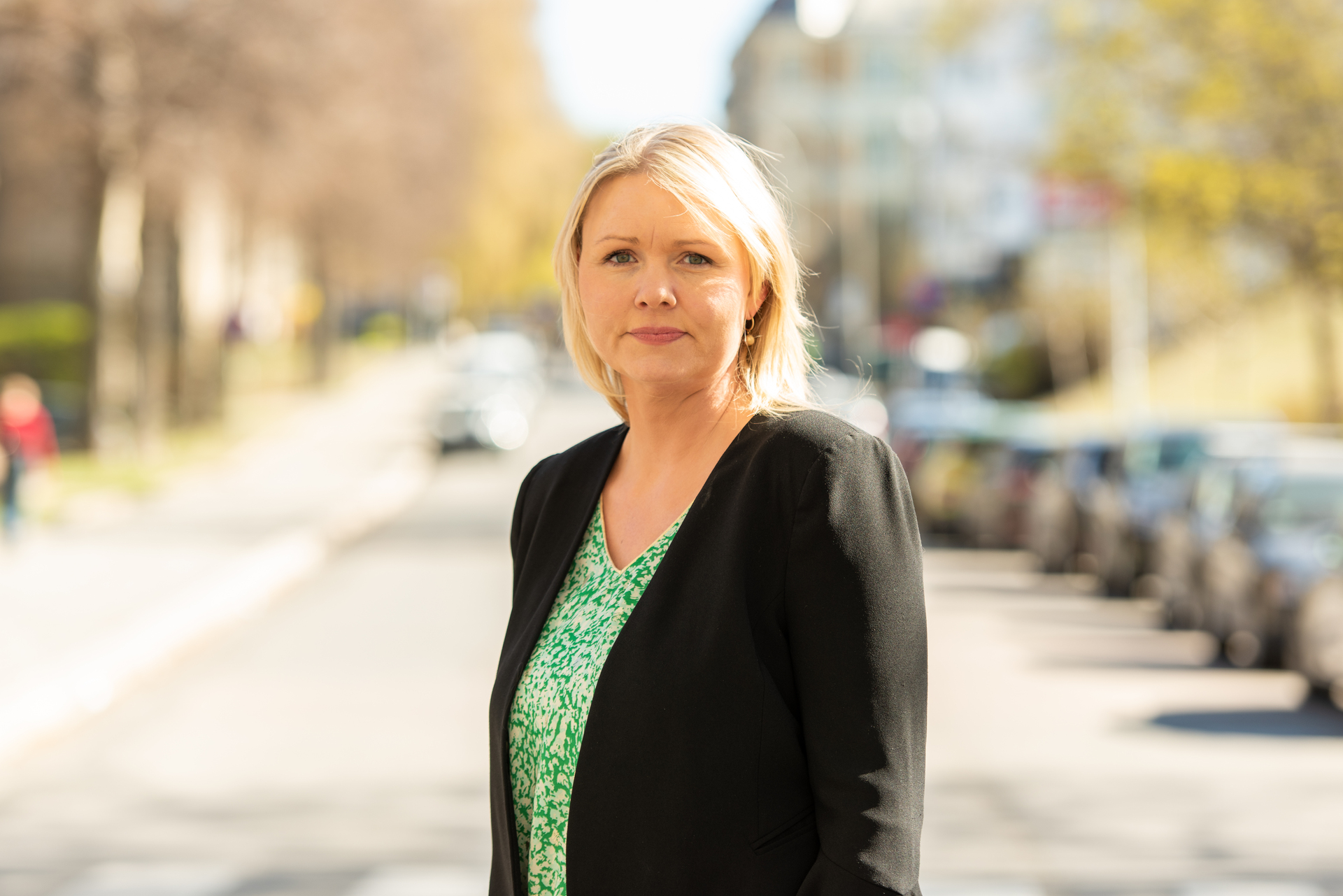 Blond kvinne står ute. Har på seg grønn topp og sort cardigan