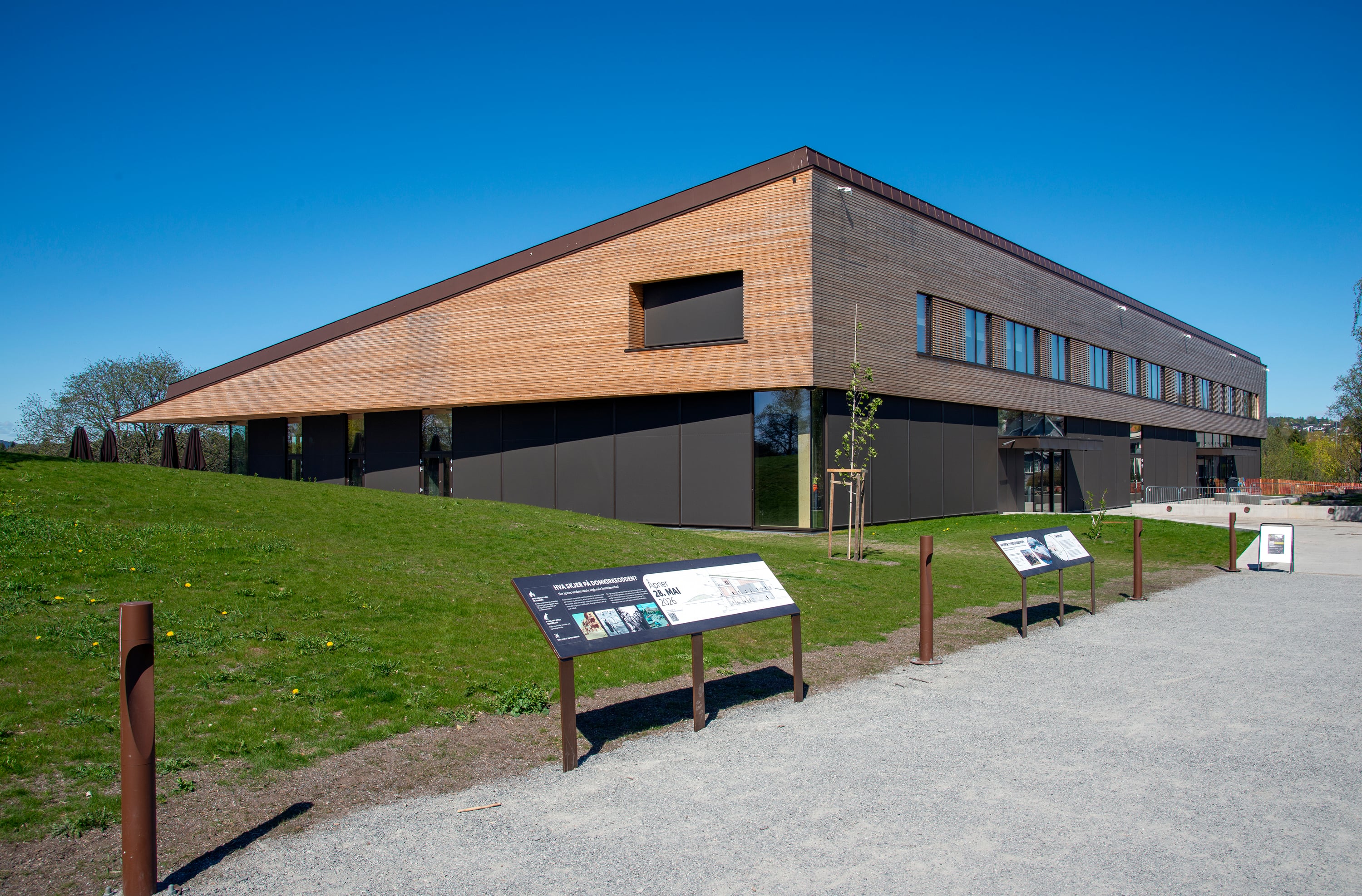 Bilde av det nye regionale historiesenteret på Domkirkeodden med skilt i forgrunnen. Lavt trehus med vinduer. Bildet er tatt mot et hjørne av huset. Kredit: Geir Ove Andreassen, Anno Domkirkeodden historiesenter
