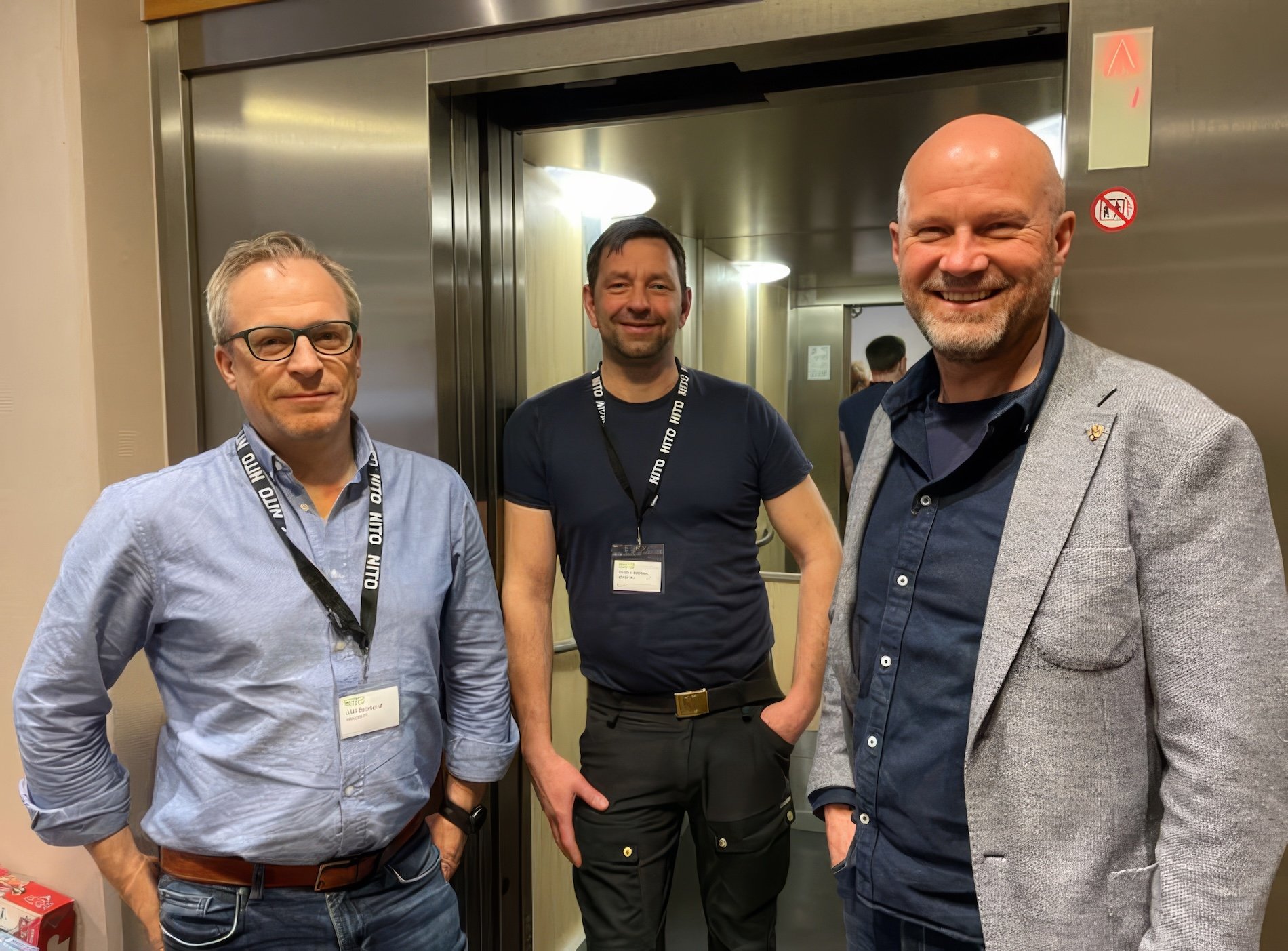 Tre menn: til venstre en mann med briller i lyseblå skjorte, mann med mørkt hår og mørkeblå t-skjorte, og til høyre mann som smiler i mørkeblå skjorte og grå blazer