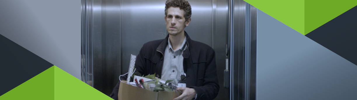Misfornøyd mann står i heisen og holder en  pappeske med personlige eiendeler.