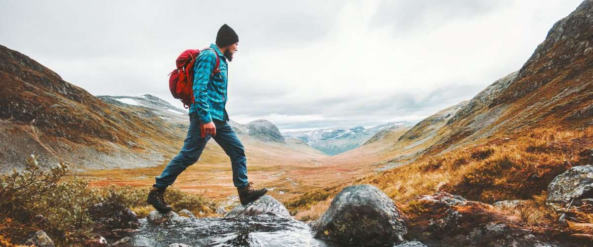 Mann på tur over en elv i fjellet. Foto: Shutterstock