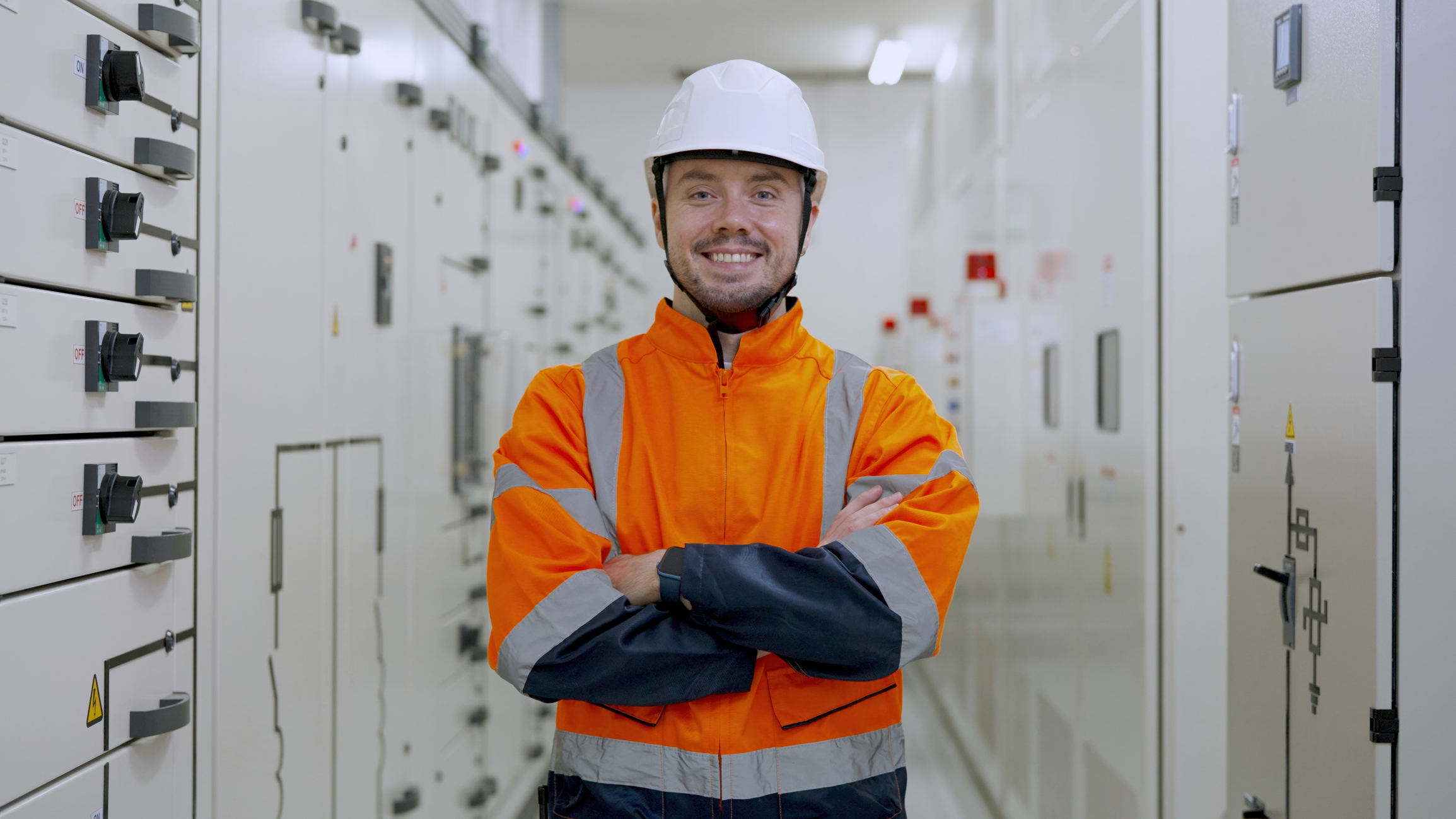 Electrical engineer stands smiling in front of electrical systems