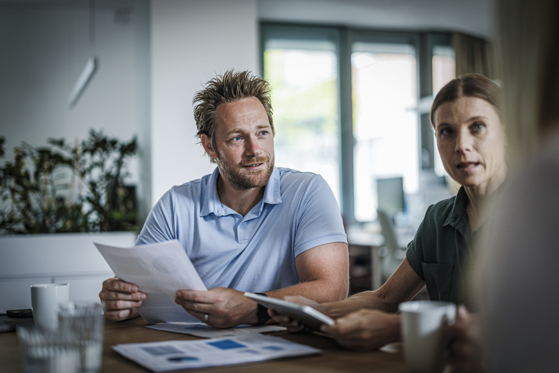 Tre ansatte snakker med hverandre og holder i papirer. 