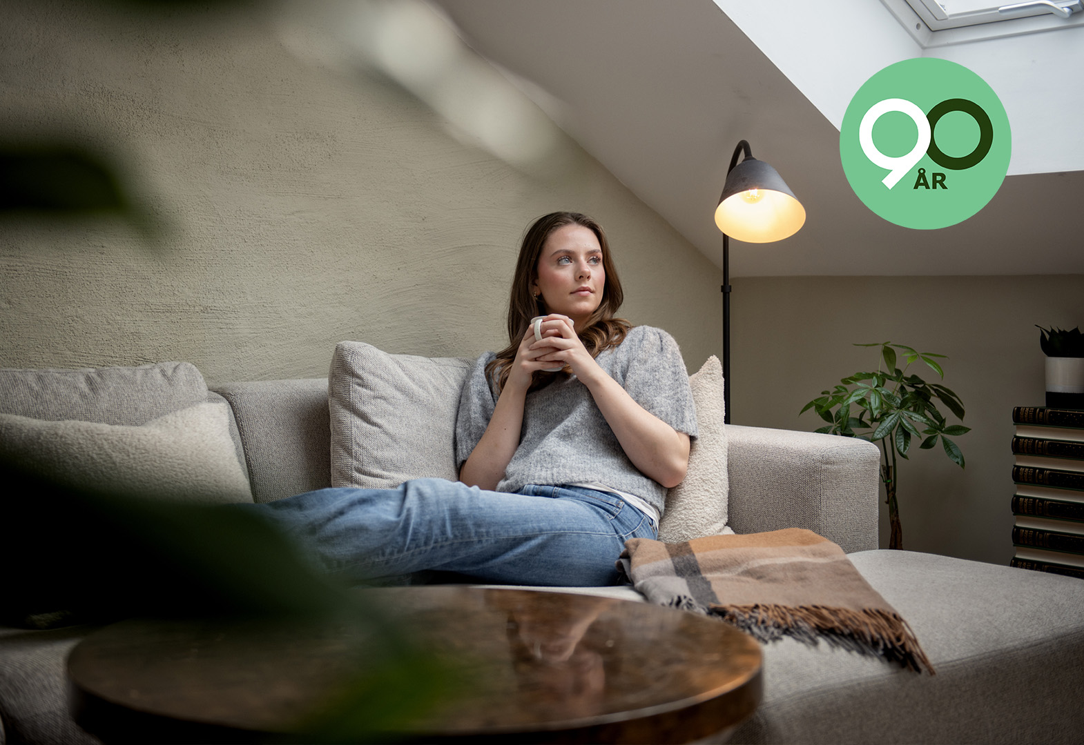 Bilde av en ung student som sitter i en sofa med en kaffekopp. Hun ser ut mot vinduet.