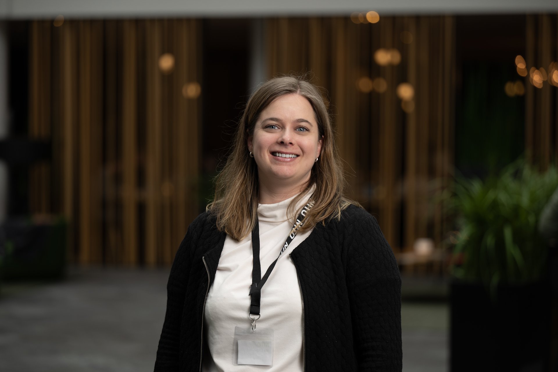 Smilende kvinne med halvlangt brunt hår, hvit genser og sort jakke