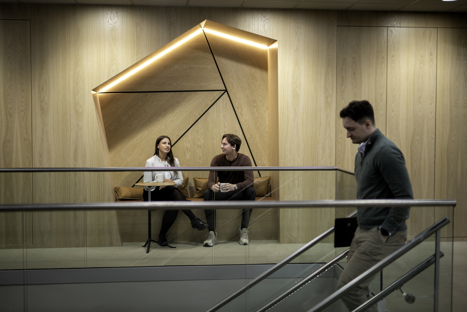 A male employee leaves his job down a flight of stairs with a non-competition clause. Two colleagues are sitting in a relaxed office space in the background.
