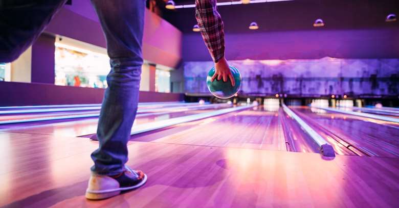 person triller bowlingball mot mål. Lilla bakgrunn