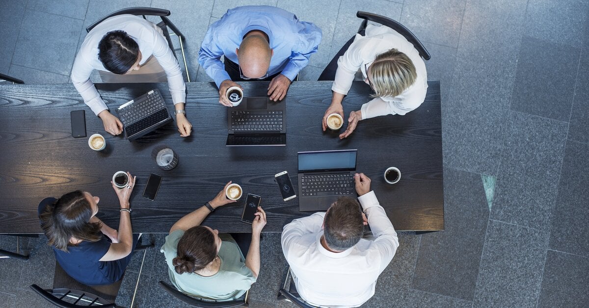 6 personer som sitter rundt et bord med hver sin pc
