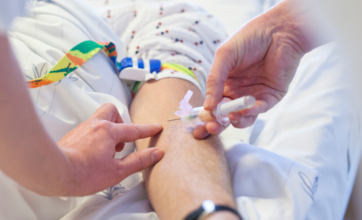 Bildet viser en helsearbeider som tar en blodprøve ved å føre en nål inn i en pasients arm.