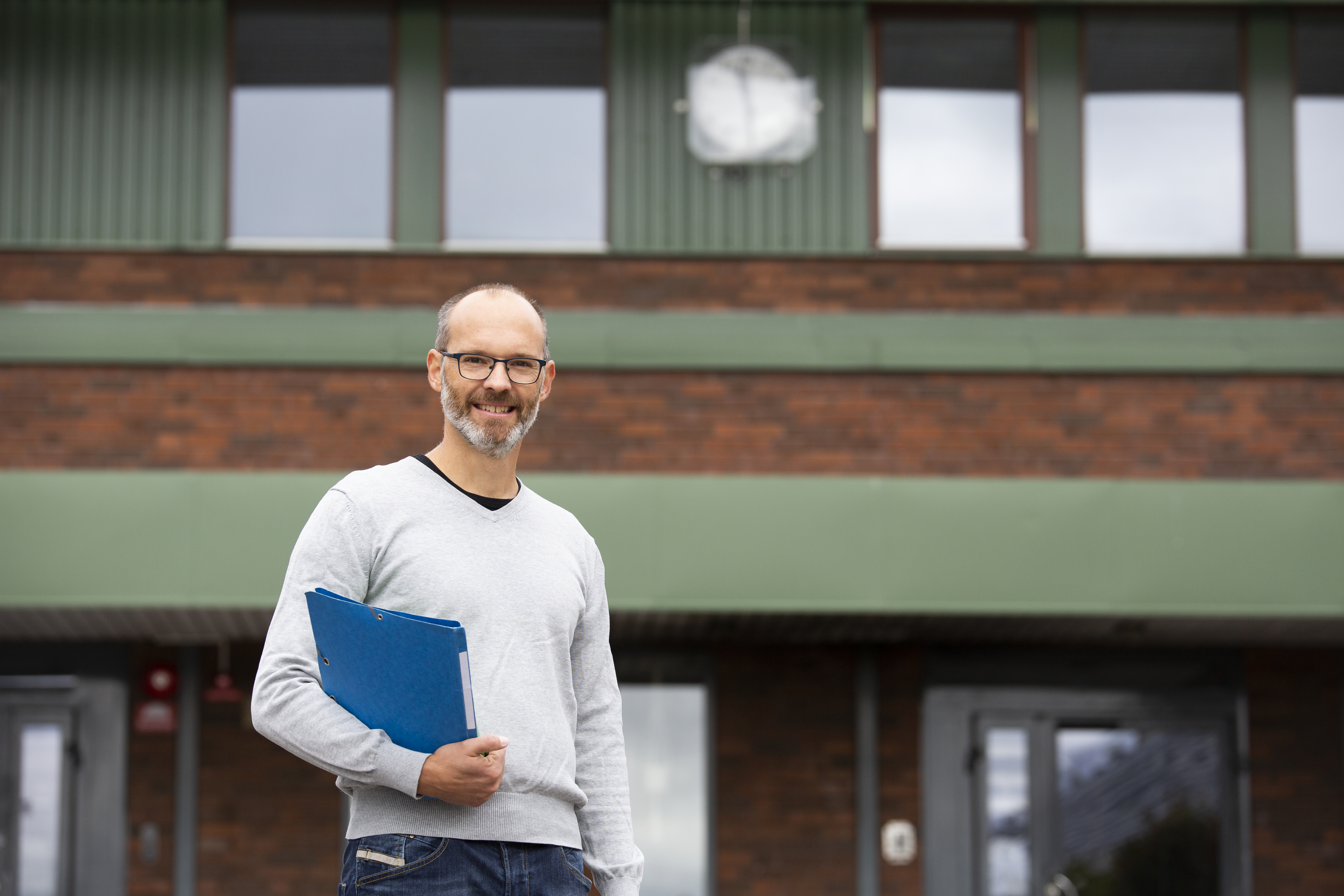 Mann som står foran skolebygning med klokke på veggen, illustrerer arbeidstid