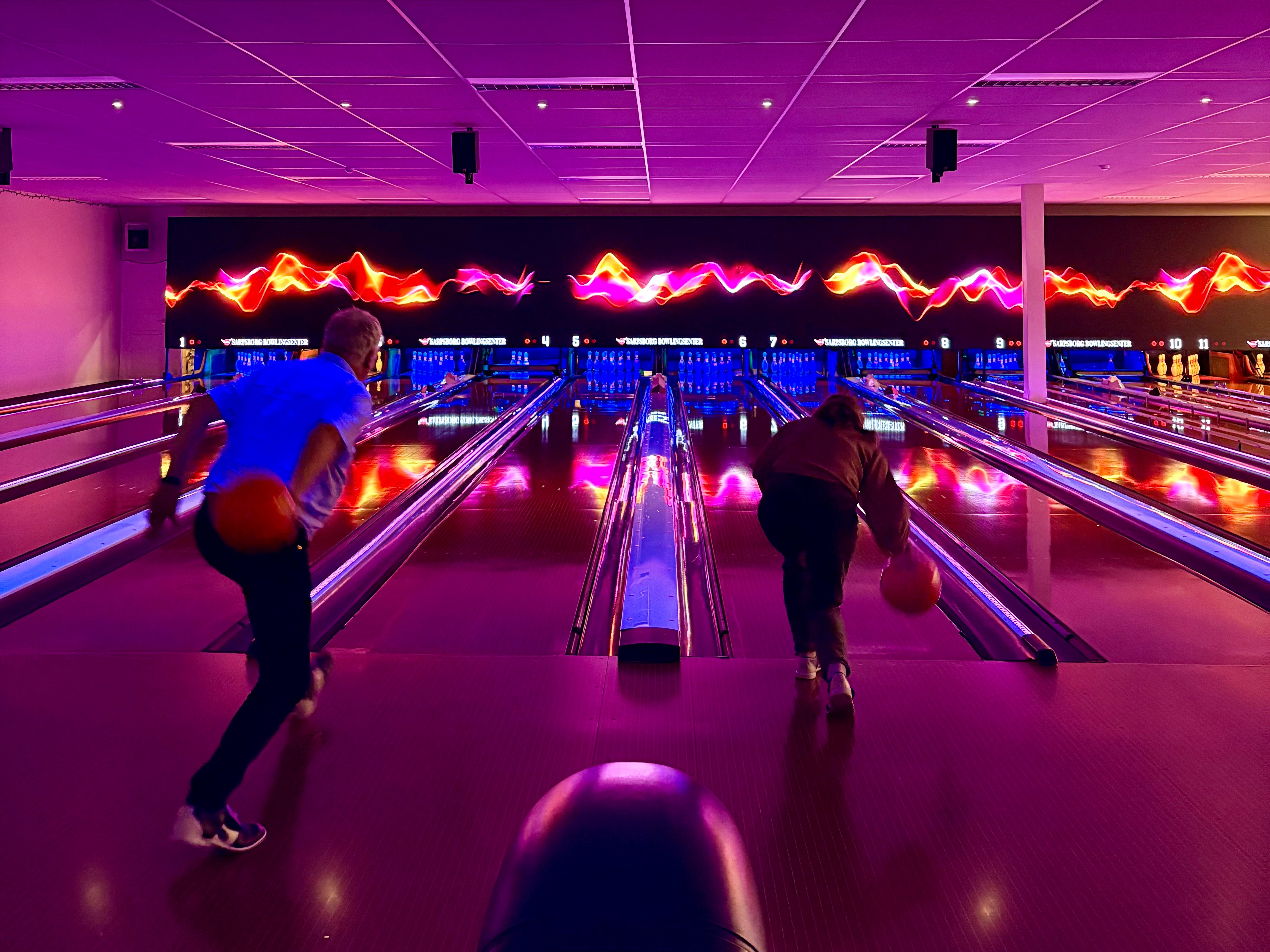 To personer som spiller bowling i en hall med rosa og lilla lys