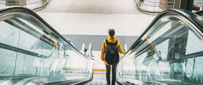 Tillitsvalgt med ryggsekk på vei opp en rulletrapp for å delta på fagforeningskurs. Illustrerer reisebestilling og personlig utvikling gjennom opplæring.