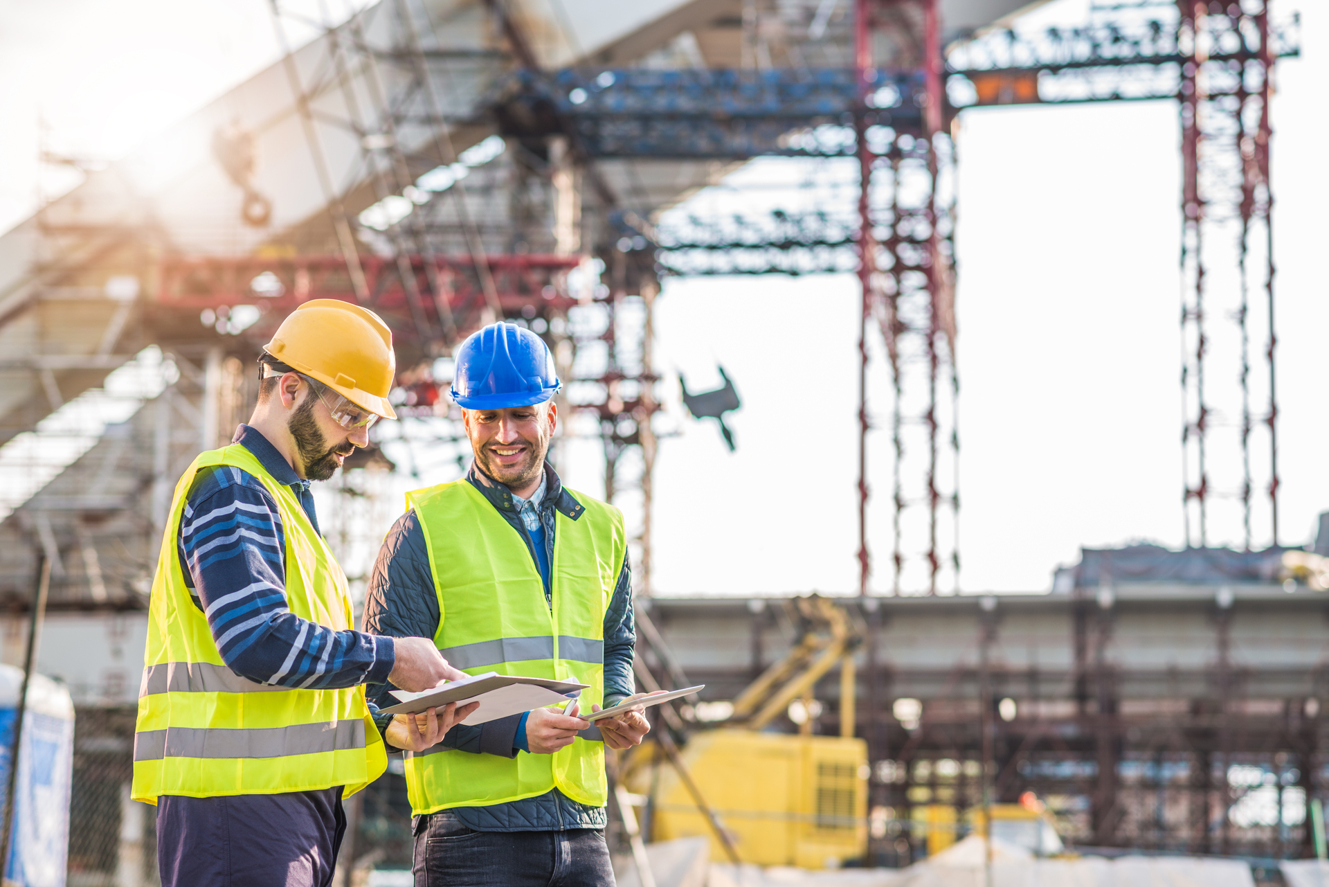 Two construction workers in protective gear discuss plans at a construction site. Illustrates cooperation and working conditions in the construction industry.