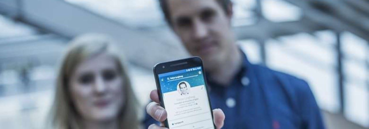 en ung kvinne og en ung mann som holder frem en mobil med linkedin hjemmesiden på skjermen