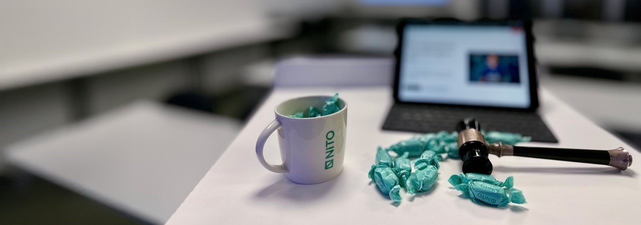 PC with screen up, NITO cup, candies and a club on the table.