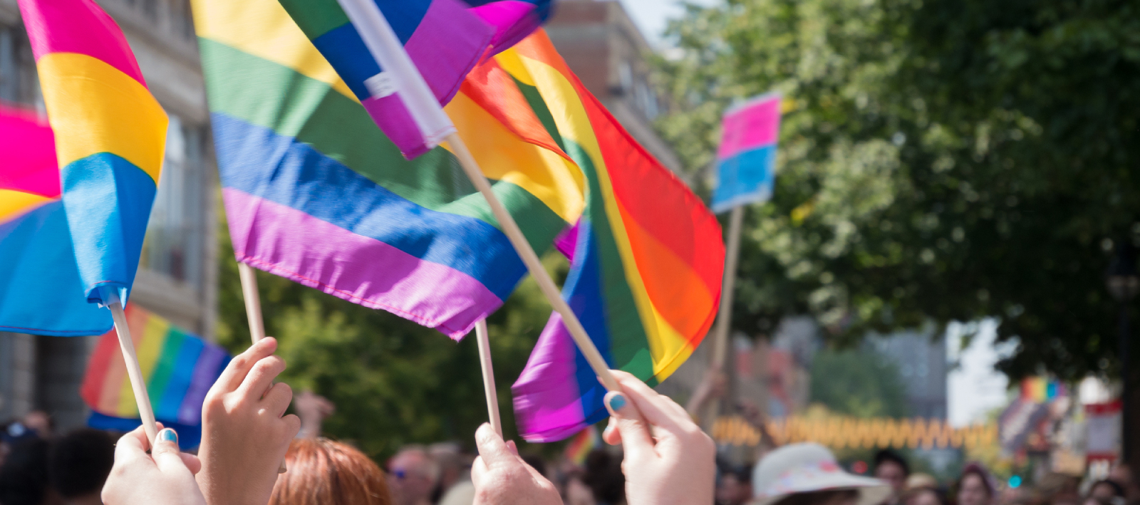 Prideflagg fra en parade. Man ser flere flagg og mennesker som går i tog.