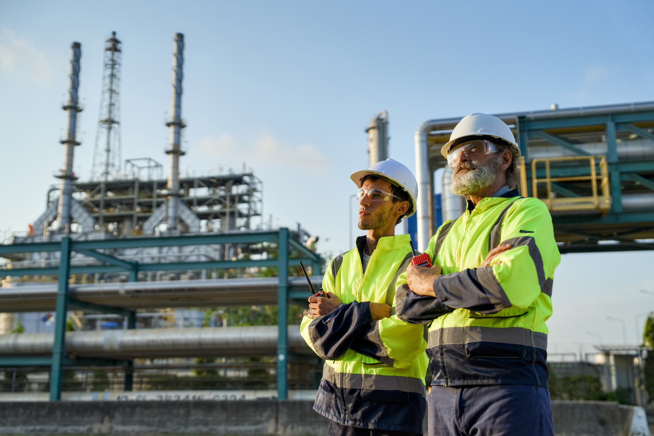 Technical personnel in protective equipment in front of industrial processing plant with pipes and installations