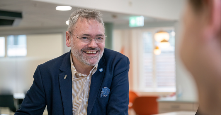 En smilende forhandlingssjef i NITO, Knut Aarbakke, med skjorte og jakke i et kontorlandskap