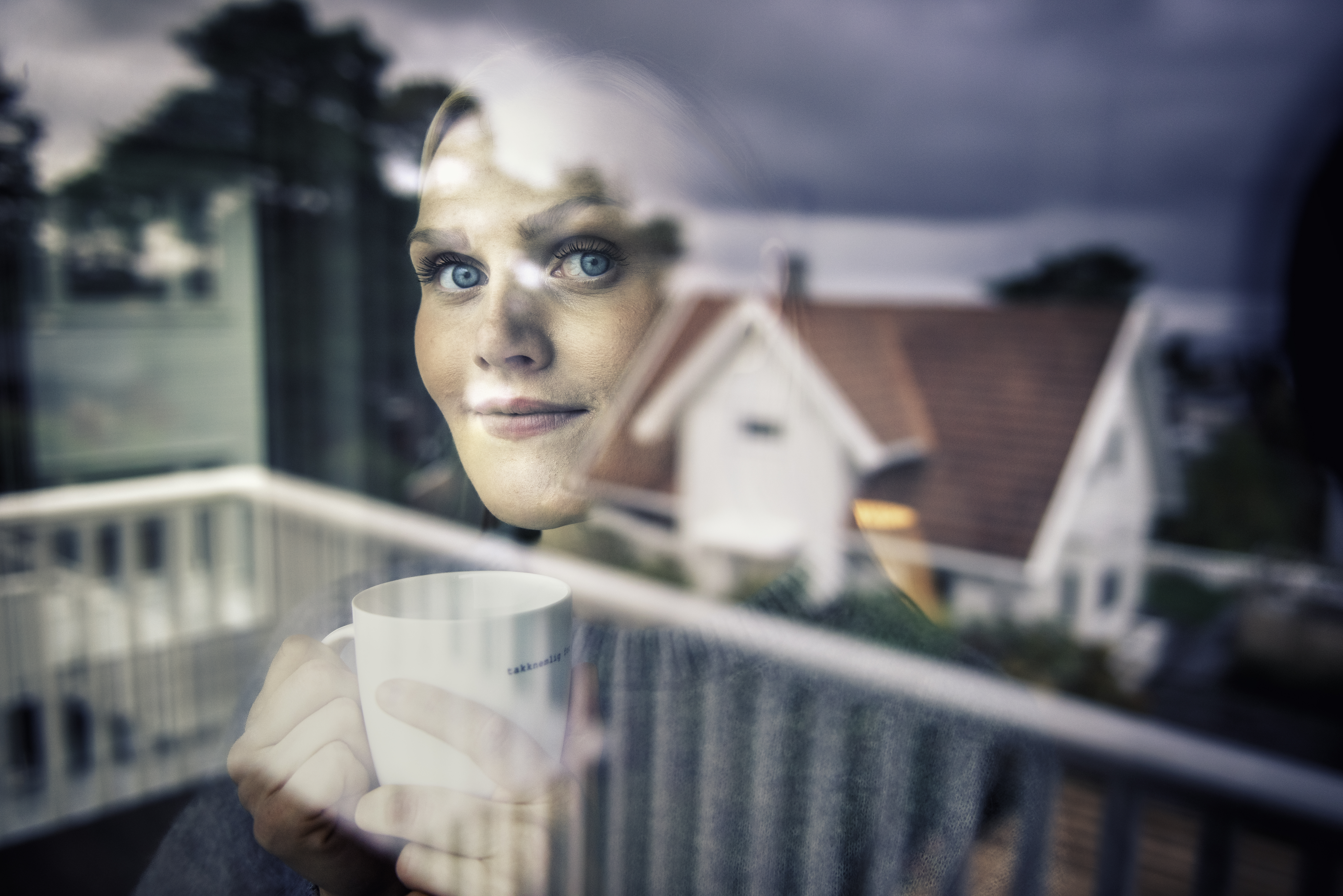 Dame som titter ut av vinduet og du ser et hus i refleksjonen