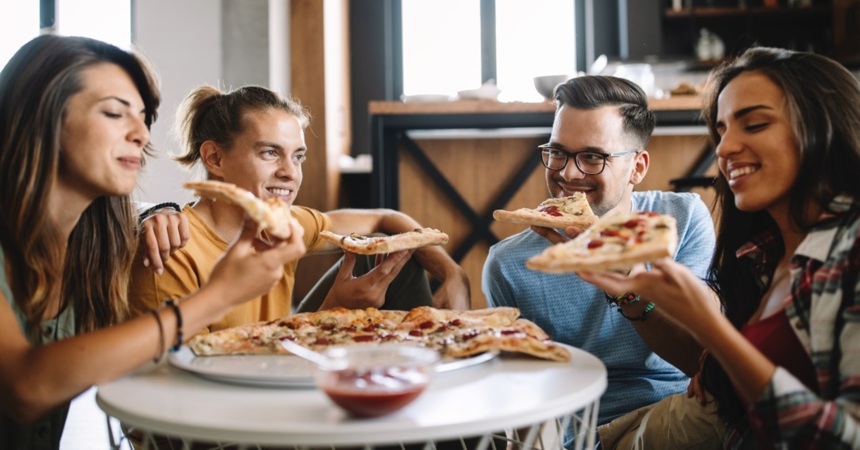 Fire personer som sitter rundt et bord og spiser pizza