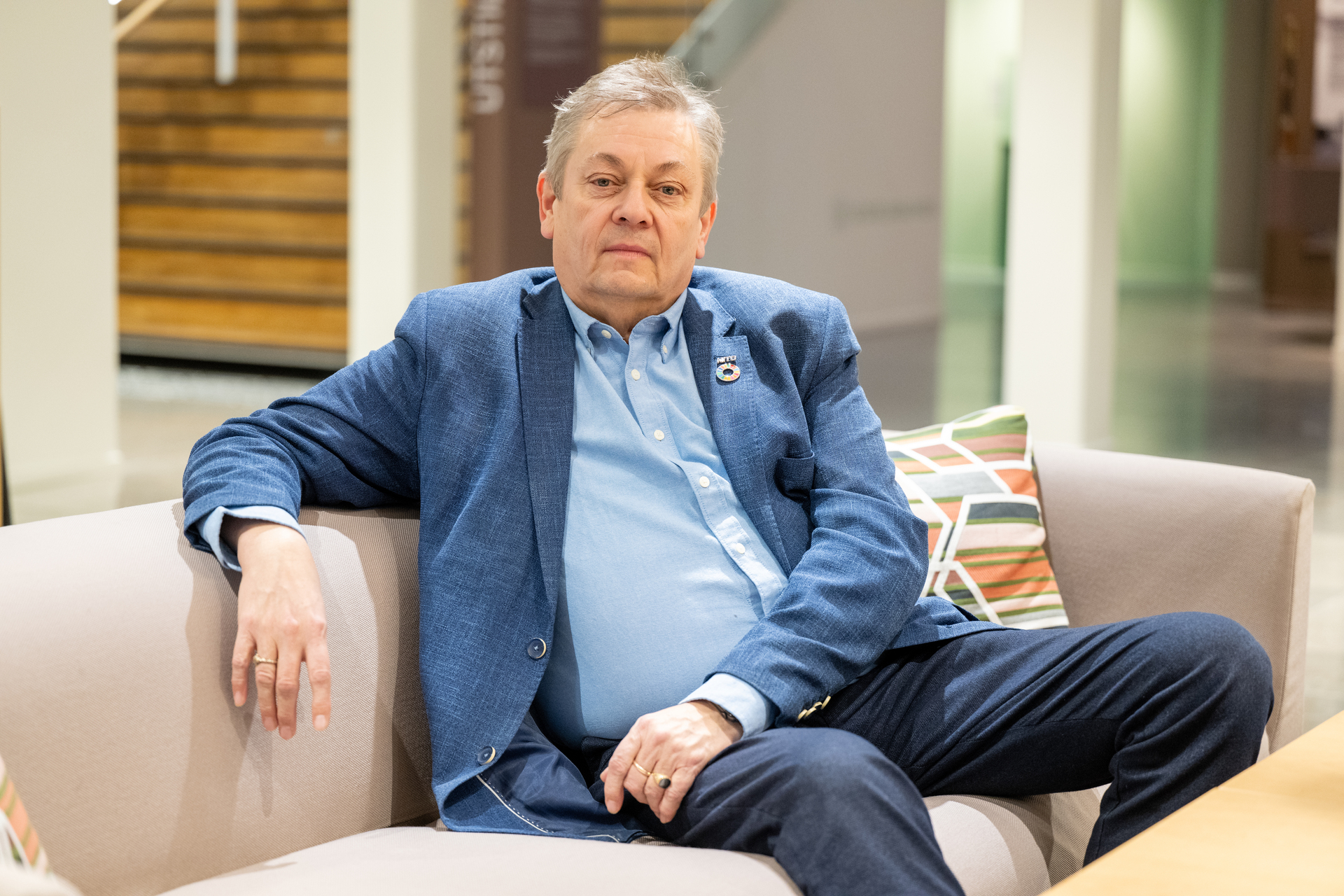 Man with a blue blazer and light blue shirt sitting on a sofa.