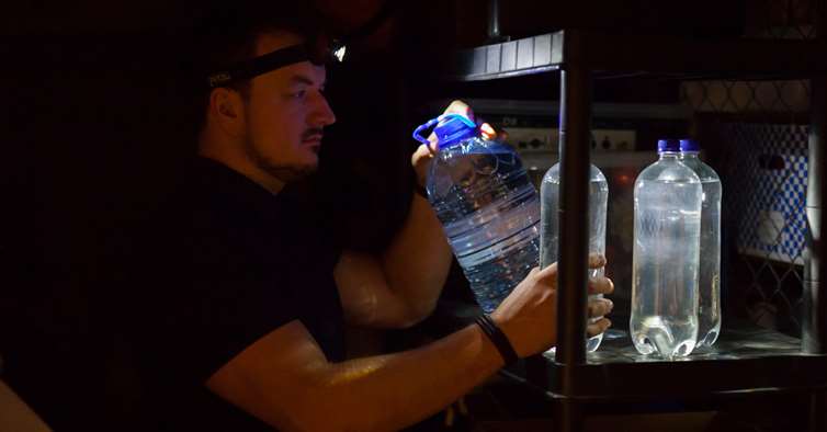 Mann i mørket med vannflasker på egenberedskapslager. 