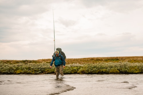 Mann med fiskeutstyr går over vannet på vidda.