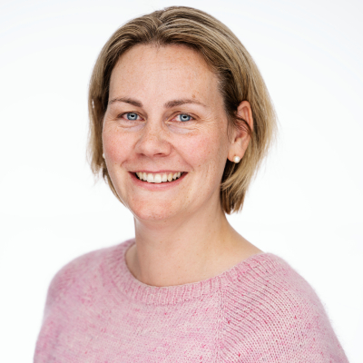 Kvinne med kort blondt hår, iført en rosa genser, mot en lys bakgrunn.