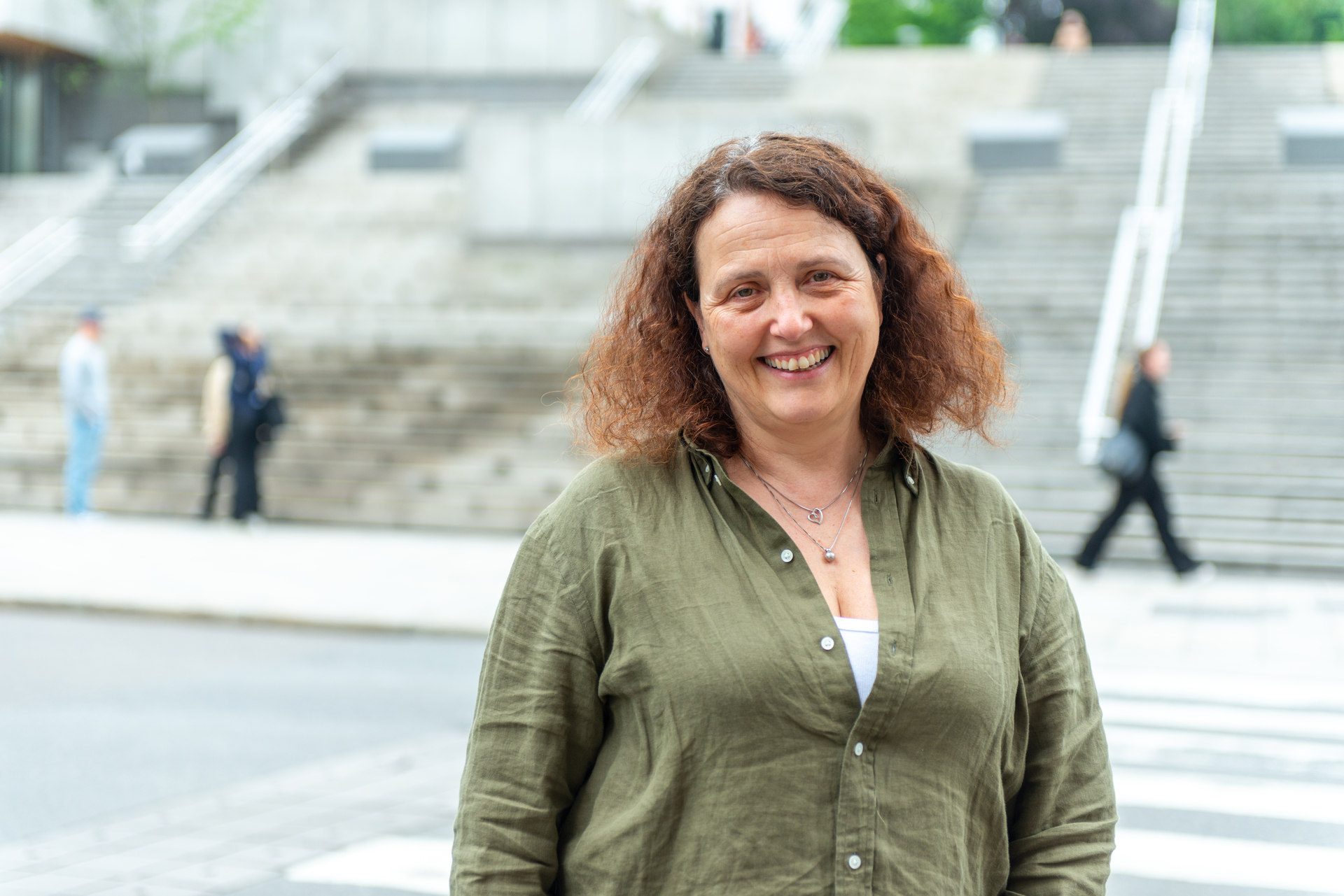 Bilde av smilende kvinne med krøllete brunt hår. Bildet er tatt utendørs.