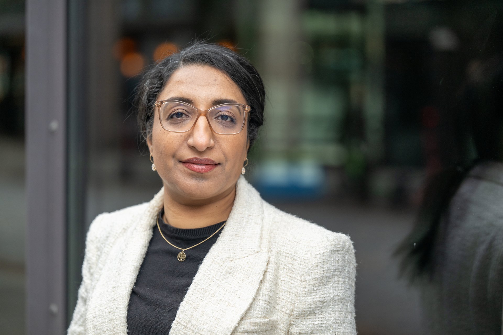 Kvinne med brunt hår og briller. Har på seg hvit jakke og sort t-skjorte