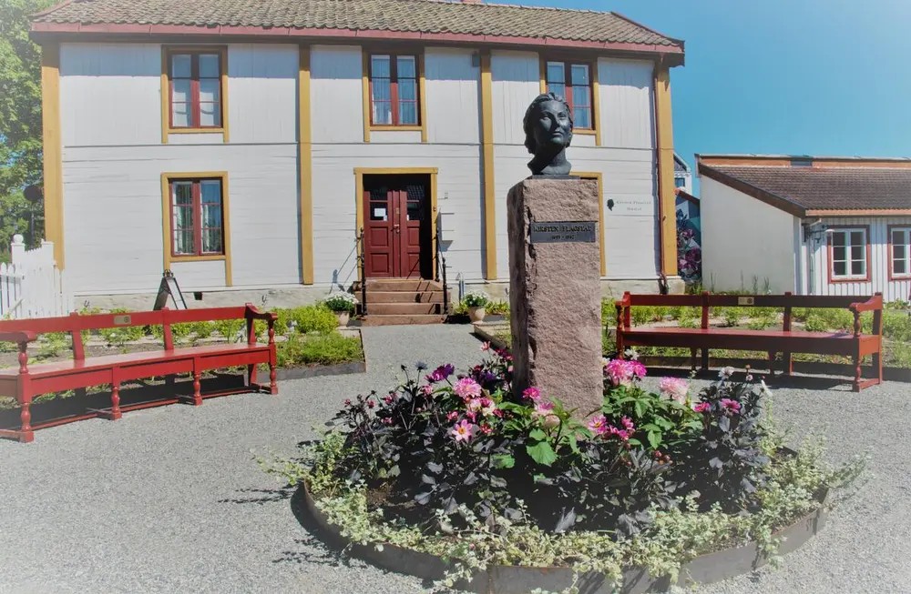 Bilde av museet med byste av Kirsten Flagstad omkranset av blomster i forgrunnen.