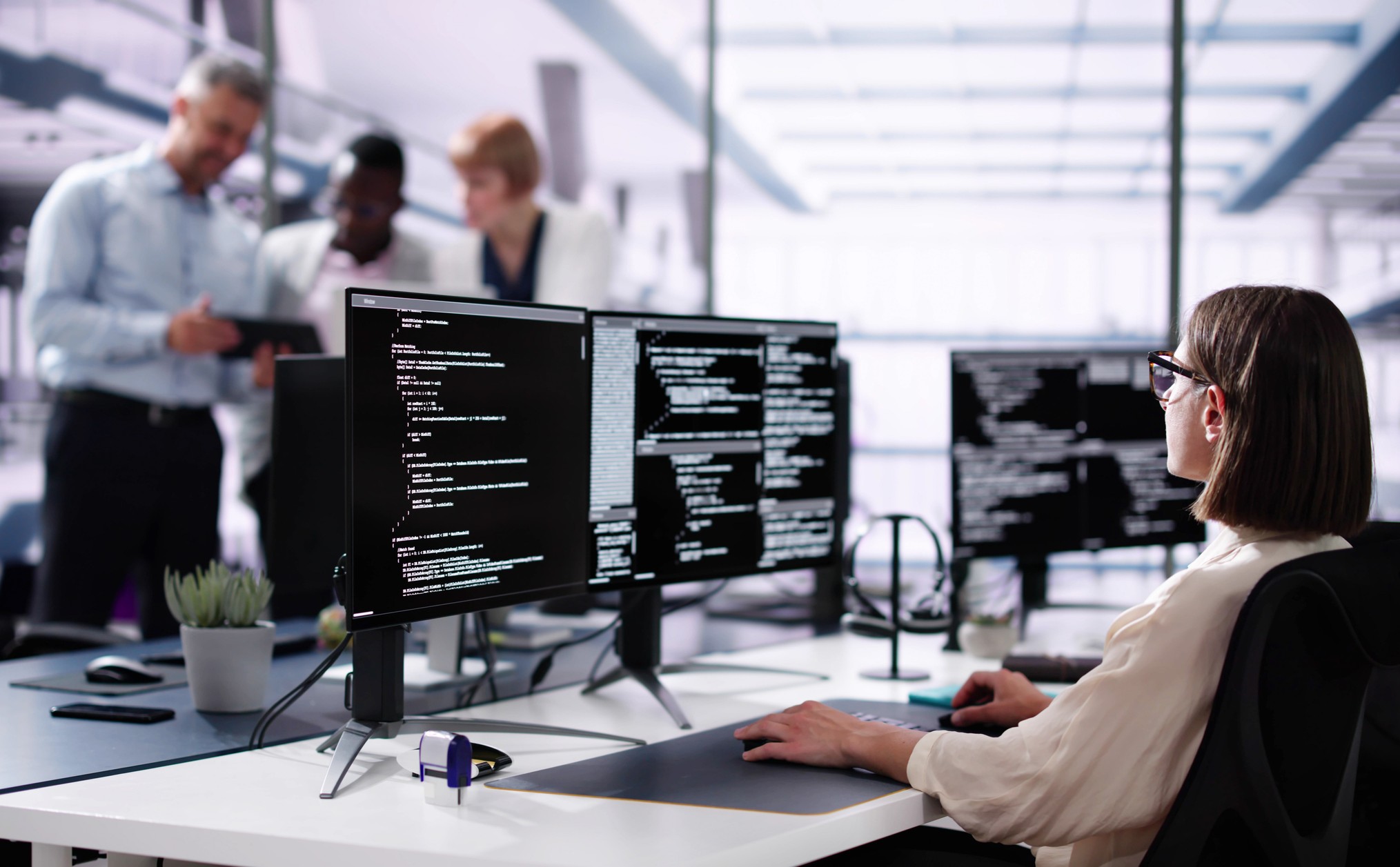 Person overvåker skjermer, kolleger i bakgrunnen